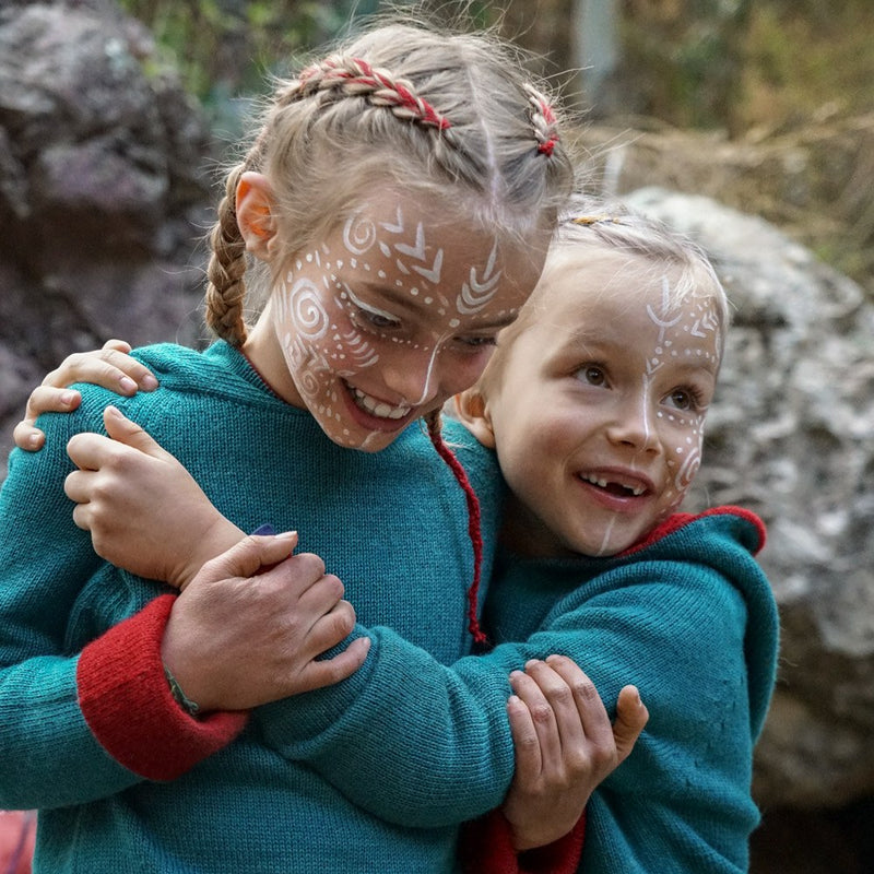 girls hugging each other with painted faces and baby alpaca clothes