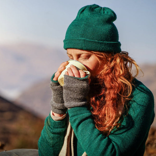 Woman drinking a cup of tea and wearing baby alpaca sweater, beanie, scarf and gloves