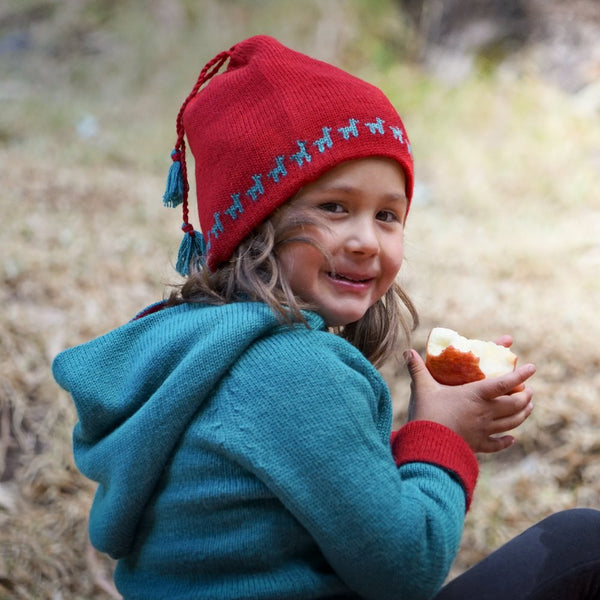 Girl with red colored baby alpaca wool hat and blue colored hoody