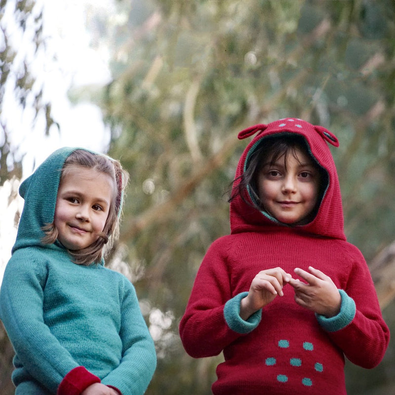 Two girls wearing baby alpaca sweater with hood in the colors blue and red